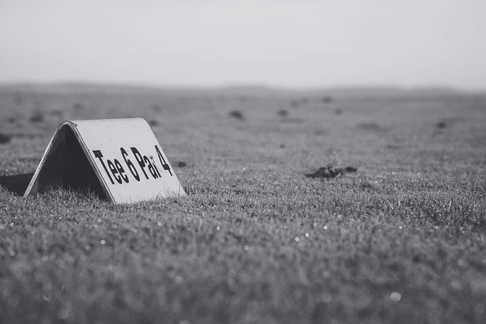 A course sign standing in a grass meadow under flat light