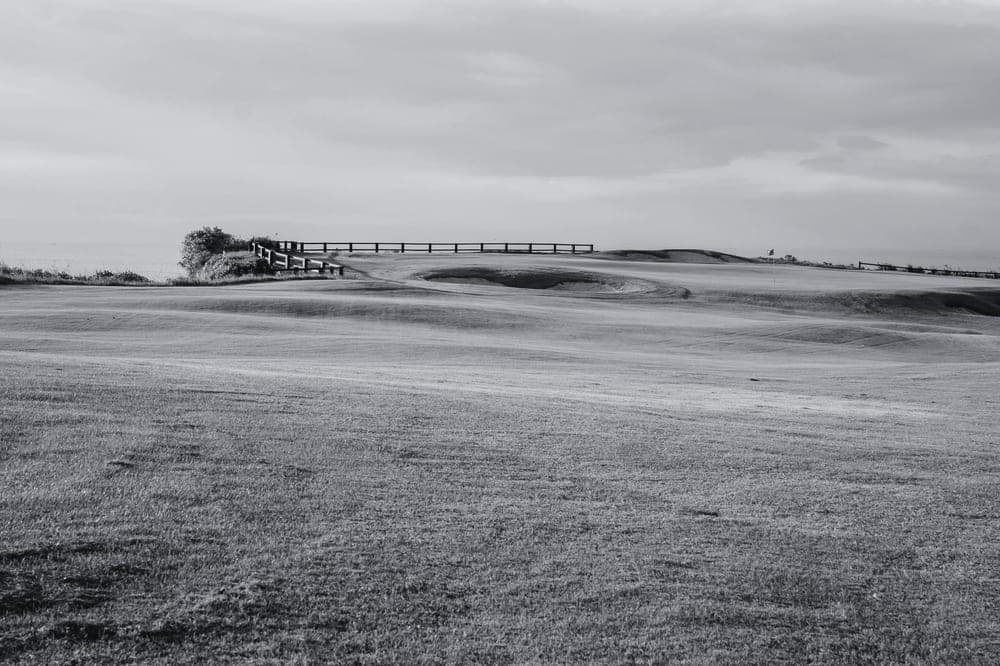 A green fairway with a boundary fence under overcast light