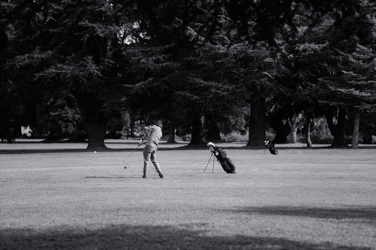 A disc golf player mid-throw on a wooded fairway under overcast light