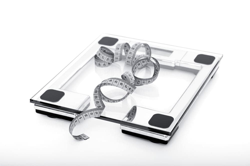 A measuring tape and weighing scale on a plain surface